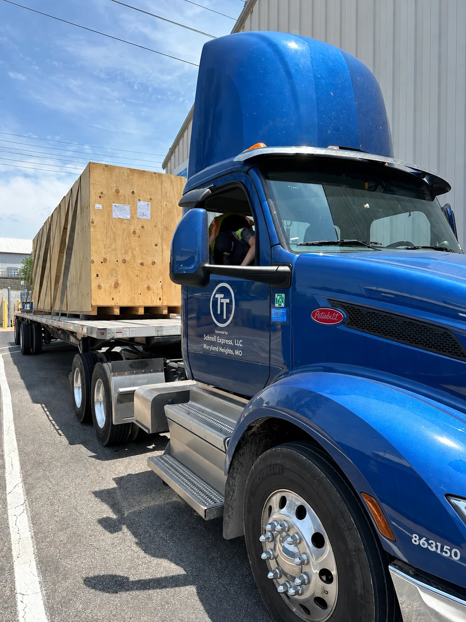 A blue T&T tractor carrying large wooden freight crates on a flatbed